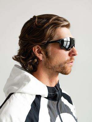 Man wearing a white and black jacket with reflective sunglasses on a light gray background
